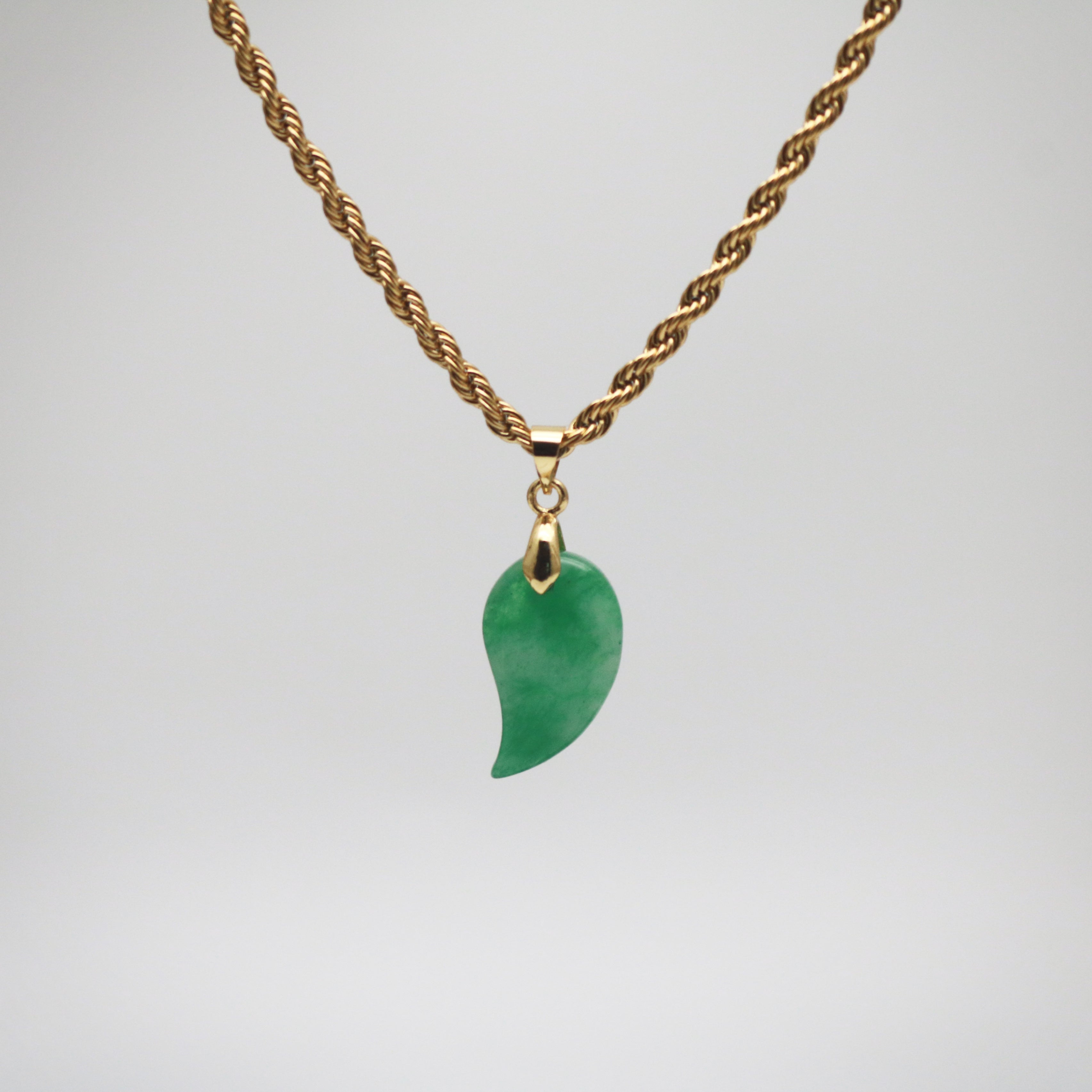 green jade pendant in comma shape hanging from a gold rope chain